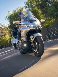 A sleek silver motorcycle parked on a sunlit road with greenery in the background.